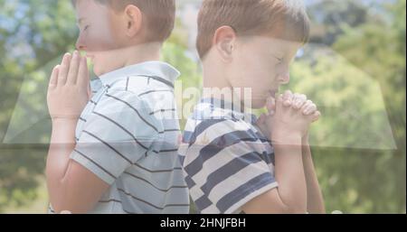 Esposizione multipla dei ragazzi elementari caucasici che pregano contro gli alberi e la bibbia sul tavolo Foto Stock