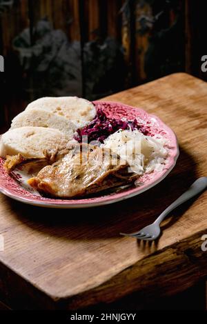 Zampe d'anatra al forno con pezzetti di pane bollito a fette, crauti rossi e bianchi in piastra di ceramica su tavolo di legno marrone. Ceco tradizionale, tedesco e ue Foto Stock