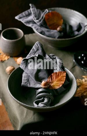 Tavolo di Halloween o Thanksgiving autunnale scuro con vasellame in ceramica artigianale vuoto, ciotole grezze e tazze su tovaglie di lino con giallo autunnale Foto Stock