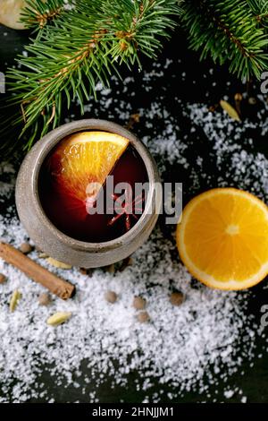 Tradizionale VIN brulé caldo in tazza di ceramica con spezie, arance e entourage natalizio su sfondo di legno nero con abete e neve. Disposizione piatta, Foto Stock