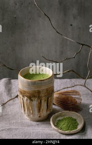 Tradizionale matcha giapponese caldo verde frothy tè in tazza di ceramica fatta a mano, matcha in polvere e whisk di bambù in piedi su tovaglia di lino grigio. Sano Foto Stock