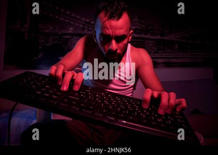 Un giocatore di trent'anni con una tastiera in mano gioca al computer, si arrabbia, si sente indignazione, varie emozioni. Vista dal lato TV. Foto Stock