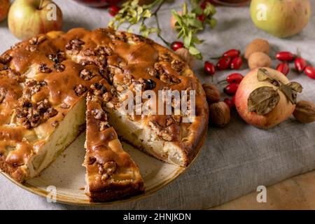 Torta fatta in casa di mele e noci Charlotte sul piatto con mele da giardinaggio fresche, cinnamons e noci intorno su tela da tavola grigia lino. Bak casa autunnale Foto Stock