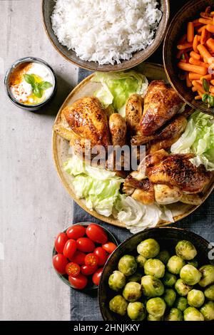 Tavolo da pranzo con pollo alla griglia, riso e verdure con germogli di brussel cotti al forno, carota per bambini in ciotole di ceramica su tovaglia di lino blu su backgrou grigio Foto Stock