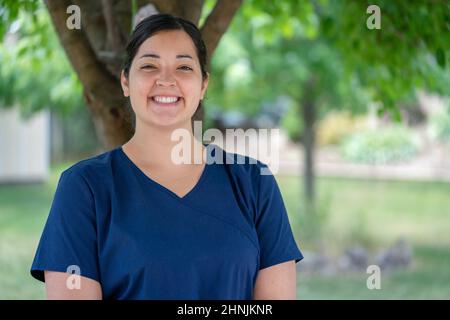Bella, femmina, essenziale, prima linea home lavoratore sorridente. Operatore sanitario personale a lungo termine con scrub medici blu marino in Canada. Foto Stock
