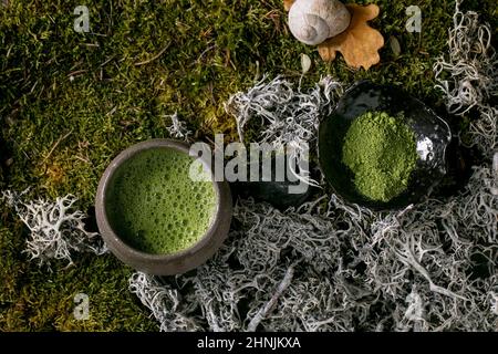 Tradizionale matcha giapponese caldo verde frothy tè in tazza di ceramica e matcha in polvere su muschio foresta come sfondo. Sana bevanda naturale. Vista dall'alto Foto Stock