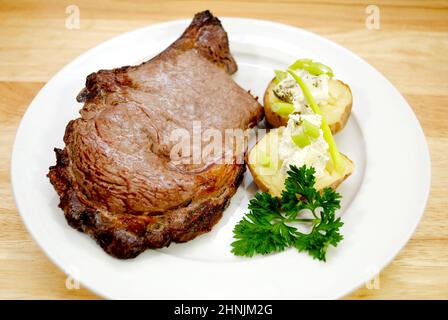 Una bistecca di costolette alla griglia servita con patate al forno e scalini Foto Stock