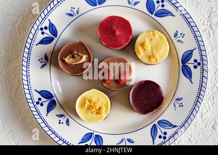 Biscotti di Natale vegani crudi al mirtillo, lampone, limone, goji e banana su un piatto con ornamenti blu Foto Stock