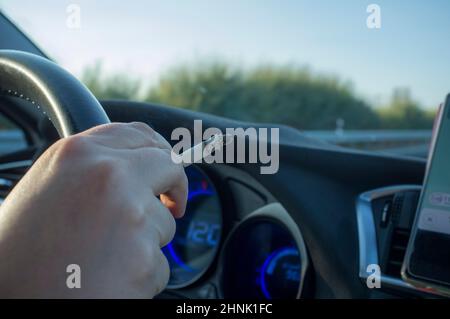 Donna che fuma durante la guida. Concetto di causa di incidenti stradali distratti. Vista interna dell'auto Foto Stock