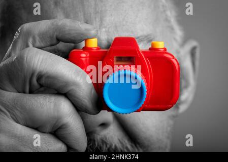 primo piano dell'uomo di mezza età in bianco e nero scatta una foto con la macchina fotografica giocattolo a colori Foto Stock