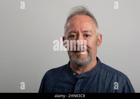 Foto ravvicinata dell'uomo di mezza età, con barba e capelli grigi su sfondo grigio Foto Stock