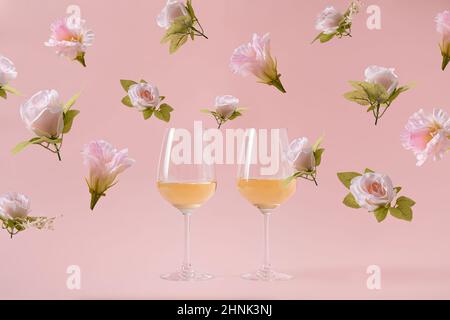 Due bicchieri di vino bianco su sfondo rosa e fiori di rosa cadenti. Concetto di festa nuziale o San Valentino Foto Stock