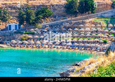 St Pauls Bay Lindos vista panoramica spiaggia con turchese mare chiaro barche turisti e sole su Rodi Grecia. Foto Stock
