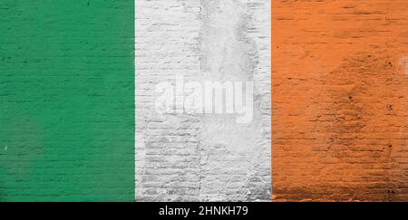 Foto full frame di una bandiera d'Irlanda intemperie dipinta su una parete di mattoni intonacati. Foto Stock