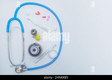 Lo stetoscopio si trova su uno sfondo bianco intorno, all'interno è un termometro, medicine, medicine e gocce da un naso che cola. Foto Stock