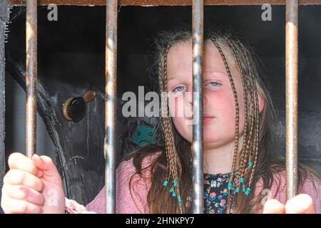 Ragazza piccola triste dietro le barre di ferro. Bambina dietro le sbarre. Concetto di violenza Foto Stock