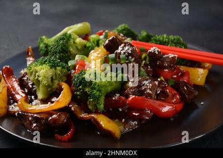 Manzo teriyaki asiatico con peperoni rossi e gialli, broccoli e semi di sesamo su un piatto sul tavolo. Manzo teriyaki piccante friggere con le verdure Foto Stock