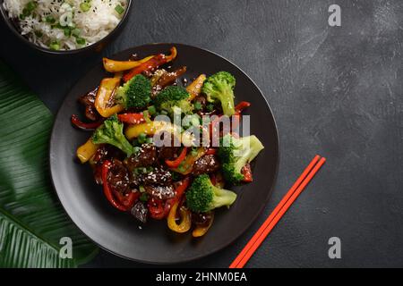 Manzo teriyaki asiatico con peperoni rossi e gialli, broccoli e semi di sesamo su un piatto sul tavolo. Manzo teriyaki piccante friggere con le verdure Foto Stock