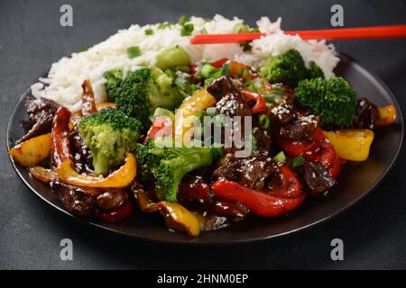 Manzo teriyaki asiatico con peperoni rossi e gialli, broccoli e semi di sesamo su un piatto sul tavolo. Manzo teriyaki piccante friggere con le verdure Foto Stock