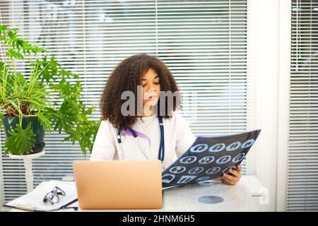 Ritratto di etnia femminile medico di analisi radiologica o MRI scansione durante il lavoro in ospedale, fuoco selettivo. Medico che guarda lo screening TC, utilizzando la diag Foto Stock