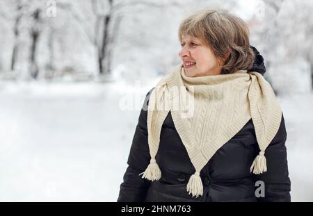 Ritratto di felice felice con clima geloso neve donna anziana in abiti caldi sorridendo alla macchina fotografica, in piedi nel parco invernale all'aperto durante il quotidiano wal Foto Stock