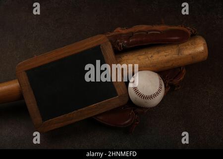 Primo piano di una vecchia palla da baseball, batè in legno, guanti vintage in pelle indossata e cartello da lavagna su sfondo marrone scuro grunge, vista dall'alto rialzata, diretta Foto Stock
