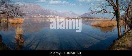 Vista panoramica su un lago alpino e sulle montagne circostanti in una giornata invernale soleggiata, Annone, Lombardia, Italia Foto Stock