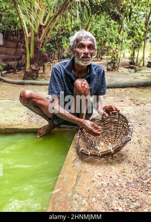 Galle, Sri Lanka - 14 aprile 2017: Uomo locale in piedi accanto al buco pieno d'acqua mostrando ai turisti come le pietre di luna (gemme semi preziose) sono riunite nella miniera di pietra di moonstone. Foto Stock