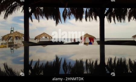 Tavola rotonda di vetro, che raffigura palme, mare e cielo. Splendida vista sulla spiaggia in una città turistica. Bar estivo sul Mar Rosso. Pergole con lettini per proteggere dal sole. Foto Stock