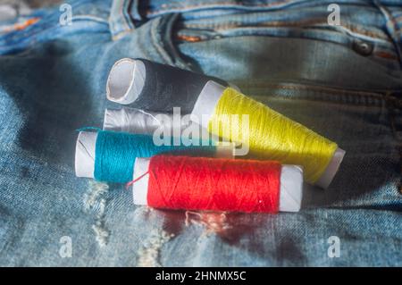 Bobine con fili da cucire colorati con jeans sullo sfondo, concetto di cucito, spazio di copia in parti dell'immagine. Foto Stock