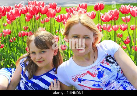 Madre con figlia sorridente vicino al letto di fiore di tulipano. Vacanze in famiglia Foto Stock