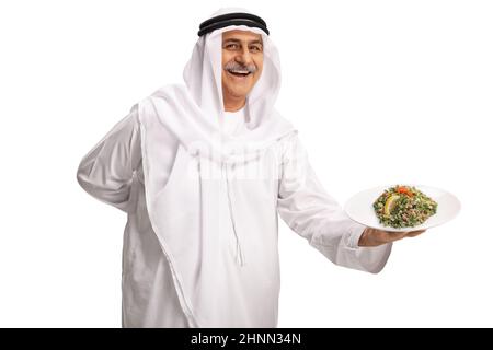 Uomo arabo maturo che tiene un piatto con insalata tabula arabo e sorridente isolato su sfondo bianco Foto Stock