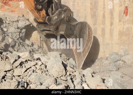 Caricamento di macerie da costruzione con un escavatore in un ambiente polveroso Foto Stock