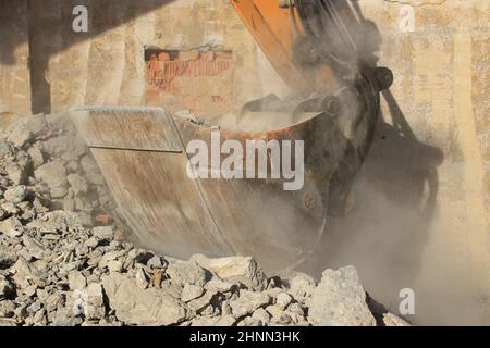 Caricamento di macerie da costruzione con un escavatore in un ambiente polveroso Foto Stock