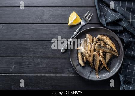 Spratti affumicati su piastra. Pesce di mare in scatola su tavola nera. Vista dall'alto. Foto Stock