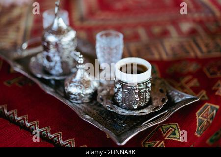 Primo piano di caffè turco servito in tazze metalliche tradizionali e bicchiere d'acqua su vassoio d'argento in un ristorante Foto Stock