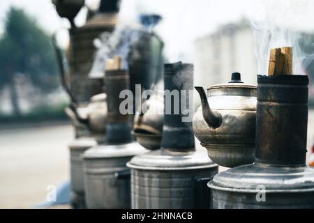 Primo piano vista prospettica fila di tradizionale tè turco samovari metallici e bollitori riscaldati all'esterno con legno ardente Foto Stock