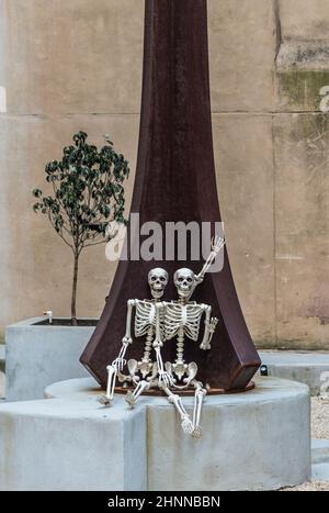 due scheletri sorridenti seduti su una panca di cemento e sorridenti Foto Stock