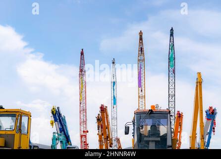 Gru mobile close-up, apripista giallo e retroescavatore blu parcheggiati in un cantiere d'asta di macchinari di seconda mano contro il cielo blu. Macchinari pesanti in affitto e vendita. Concessionaria gru per edilizia. Foto Stock