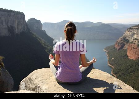 Vista posteriore di uno yoga pratica yoga sulla cima di una scogliera in montagna Foto Stock