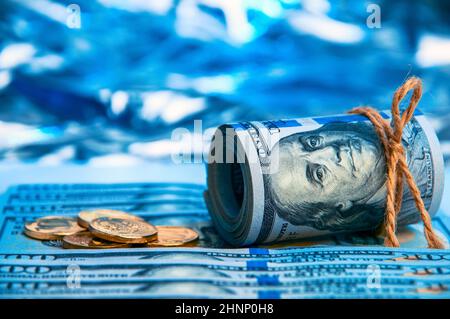 Dollari. Un rotolo di fatture del cento-dollaro e monete d'oro sparse che giacciono sulle fatture su uno sfondo blu con un lato. Stile blu. Foto Stock