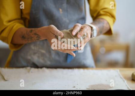 Le mani dell'artista del vasaio femminile stampano l'argilla grezza. Ceramista donna in grembiule preparare per la modellazione ceramica Foto Stock