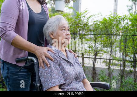La figlia del caregiver aiuta la donna anziana anziana o anziana asiatica su sedia a rotelle elettrica nel parco. Foto Stock