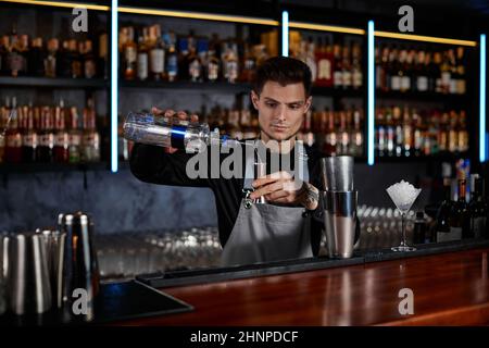 Il barista in grembiule aggiunge l'ingrediente allo shaker Foto Stock