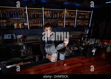 Il barman tiene in mano una paletta di metallo con cubetti di ghiaccio e li  versa in vetro vecchio stile Foto stock - Alamy