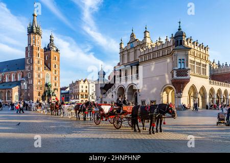 Carrozze a cavallo di fronte alla chiesa di Mariacki sulla piazza principale di Cracovia Foto Stock