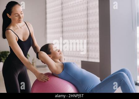 Donna incinta con un allenatore durante le lezioni di fitness con una palla Foto Stock