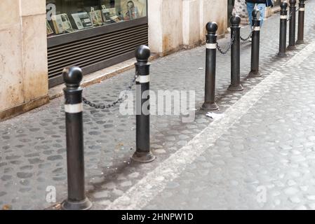 Montanti anti-parcheggio con catene. I pali di metallo separano il marciapiede e la carreggiata sul marciapiede di ciottoli. Foto Stock
