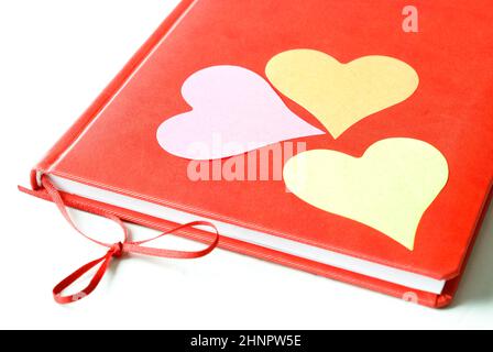 Tre note adesive a forma di cuore appiccicate al diario rosso isolato su sfondo bianco. San Valentino e concetto d'amore. Foto Stock