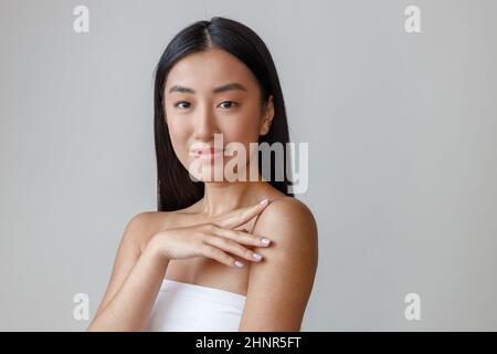 Giovane donna asiatica che tocca la spalla e sorride Foto Stock